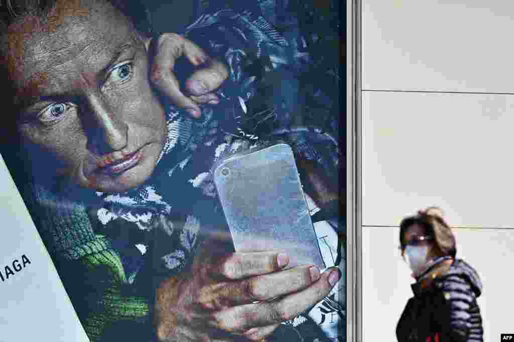 A woman wearing a face mask walks past an advertisement along a street in Tokyo&#39;s Yurakucho area.