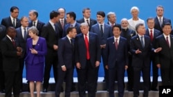 President Donald Trump, front center, listens to France's President Emmanuel Macron as they pose with world leaders for a group picture at the start of the G20 Leader's Summit inside the Costa Salguero Center in Buenos Aires, Argentina, Friday, Nov. 30, 2