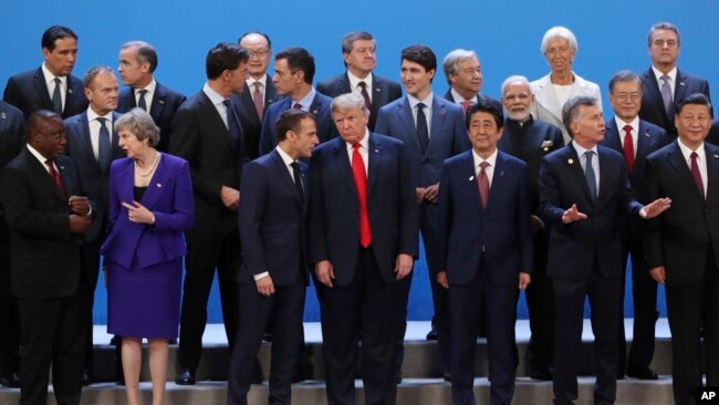 President Donald Trump, front center, listens to France's President Emmanuel Macron as they pose with world leaders for a group picture at the start of the G20 Leader's Summit inside the Costa Salguero Center in Buenos Aires, Argentina, Friday, Nov. 30, 2