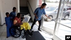 Ali Said, of Somalia, leaves a center for refugees with his two sons, as refugee caseworker Mohamed Yassin, right, holds open the door, July 6, 2017, in San Diego. Said, whose leg was blown off by a grenade, says he feels unbelievably lucky to be among the last refugees allowed into the United States before stricter rules kick in as part of the Trump administration's travel ban. 