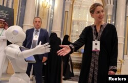 FILE - Aurore Chiquot of SoftBank Robotics Europe extends her hand to a robot during the Future Investment Initiative conference in Riyadh, Saudi Arabia, Oct. 25, 2017.