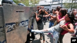 A woman kicks at a riot police shield as relatives of prisoners wait to hear news about their family members imprisoned at a police station where a riot broke out, in Valencia, Venezuela, Wednesday, March 28, 2018.