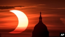 In this photo provided by NASA, a partial solar eclipse is seen as the sun rises to the left of the U.S. Capitol in Washington, June 10, 2021, as seen from Arlington, Virginia. 