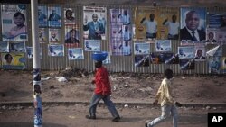 Pedestrians walk past election posters in Democratic Republic of Congo's capital Kinshasa, November 25, 2011.