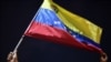 Un hombre mueve una bandera venezolana, mientras familiares y amigos de migrantes venezolanos que murieron cuando se hundió un barco que los transportaba a Trinidad y Tobago, protestan en Guiria, Venezuela. Diciembre 18, 2020. Foto: AFP.