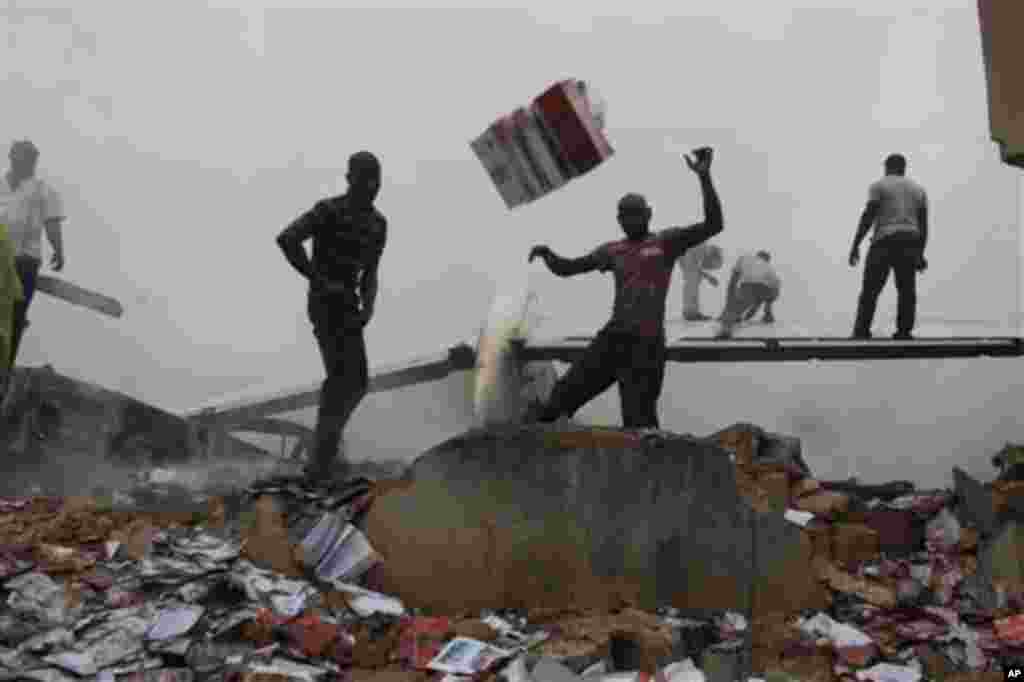 Onlookers throw debris away from the tail wing of a crashed Dana Airlines passenger plane in a neighborhood just north of Murtala Muhammed International Airport, in Lagos, Nigeria, Sunday, June 3, 2012. 