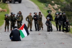 FILE - A demonstrator holds a Palestinian flag in front of Israeli forces as Palestinians protest against President Donald Trump's Mideast initiative, in Jordan Valley in the West Bank, Feb. 25, 2020.