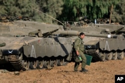 FILE - An Israeli soldier walks past tanks near the Israel and Gaza border, July 10, 2014. Israel is looking to boost the amount of money the United States sends it every year for military aid to as much as $5 billion.
