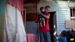 FILE - Ricardo Gonzalez holds her 8-month old daughter Keyla as his son Antonio, right, 3, talks to him at their home in the Juan Pablo II shanty town in Santiago, Chile, Jan. 23, 2013. 