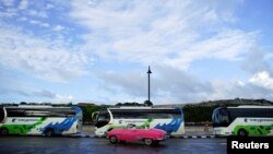 FILE - Tourists ride in a vintage car as they pass by buses owned by the Cuban military-run Gaviota tourism corporation in Havana, Cuba, Nov. 9, 2017. 