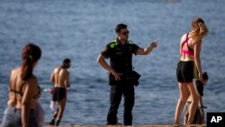 Polisi memperingatkan orang-orang untuk tidak duduk-duduk di pantai Barcelona saat Spanyol mulai melonggarkan pembatasan terkait Covid-19. 