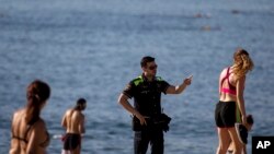  A police officer asks people to not sit while patrolling at the beach in Barcelona, Spain, Wednesday, May 20, 2020