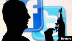 FILE - A man is silhouetted in front of a video screen with the Facebook and Twitter logos, in this picture illustration, Oct. 22, 2013.