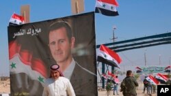 On Sept. 30, 2019, a man passes a poster of Syrian President Bashar Assad that reads, "Congratulations victory," at the newly opened crossing between the Iraqi town of Qaim and Syria's Boukamal, Syria.