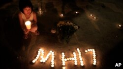 FILE - A girl holding a candle squats next to candles forming the letters MH17 during an event to mourn the victims of the crashed Malaysia Airlines Flight 17, in Kuala Lumpur, Malaysia, July 20, 2014.