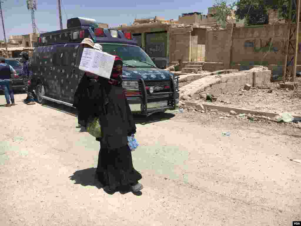 A woman passes by an Iraqi forces medical team after receiving food and water from aid groups in 17th Tamouz neighborhood in Mosul, Iraq, May 31, 2017. (K.Omar/VOA)