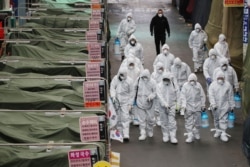 Workers wearing protective gear spray disinfectant at a market in the southeastern city of Daegu, South Korea, as a preventive measure after the COVID-19 coronavirus outbreak.