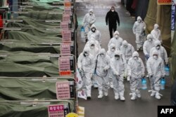 Workers wearing protective gear spray disinfectant at a market in the southeastern city of Daegu, South Korea, as a preventive measure after the COVID-19 coronavirus outbreak, Feb. 23, 2020.