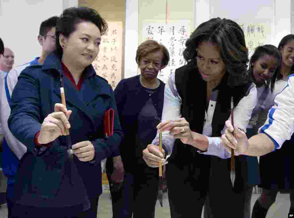 Peng Liyuan, wife of Chinese President Xi Jinping, shows U.S. first lady Michelle Obama how to hold a writing brush as they visit a Chinese traditional calligraphy class at the Beijing Normal School, March 21, 2014.