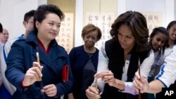 Peng Liyuan, istri President China Xi Jinping, memperlihatkan bagaimana memegang kuas kaligrafi kepada Michelle Obama dalam demonstrasi kaligrafi di sebuah sekolah di Beijing (21/3).