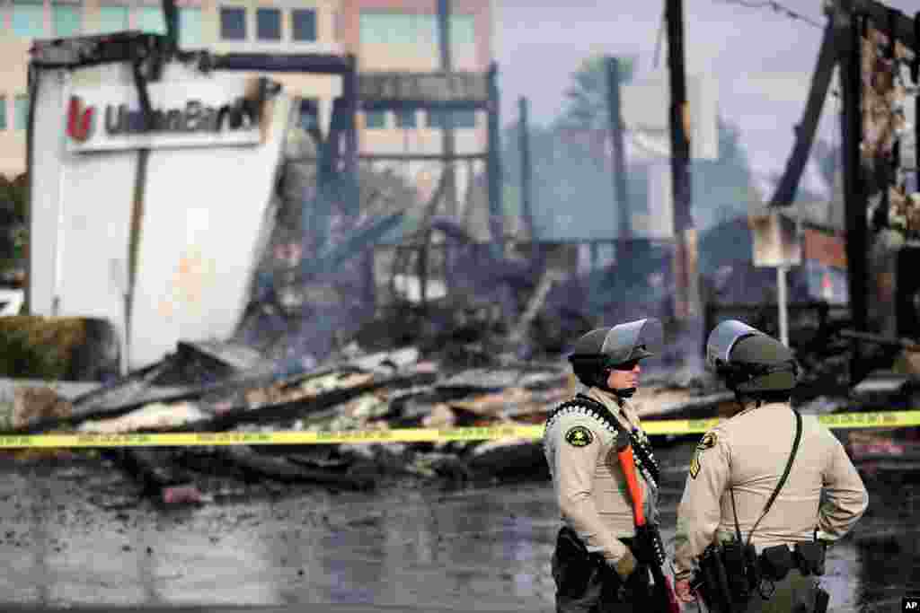 San Diego County sheriff officers stand guard in front of a burning bank building after a protest over the death of George Floyd, May 31, 2020, in La Mesa, Calif