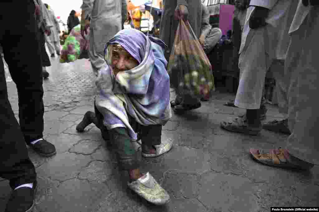 Mahta, de 70 años, se arrastra por la calle actuando como si estuviera discapacitada en el centro de Kabul pidiendo dinero. Se ve obligada a hacer esto para que los hombres que pasen sientan lástima por ella. Kabul, Afganistán. [Foto: Paula Bronstein]