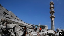 Palestinians stand in rubble of the al-Qassam mosque in Nuseirat refugee camp, central Gaza Strip, after it was hit by an Israeli airstrike, Saturday, Aug. 9, 2014.