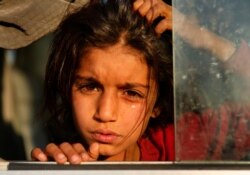 A Syrian girl who is newly displaced by the Turkish military operation in northeastern Syria, cries as she sits in a bus upon her arrival at the Bardarash camp, north of Mosul, Iraq.