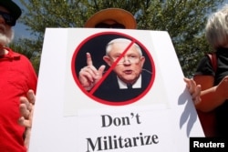 Un activista por los derechos de los inmigrantes sostiene un cartel mientras protesta por la visita del Fiscal General Jeff Sessions a la Reunión Anual de Primavera de la Coalición de Alguaciles, en Las Cruces, Nuevo México. Abril 11 de 2018.
