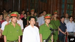 Cu Huy Ha Vu (C) stands between policemen in the dock during his trial at a court in Hanoi August 2, 21, 2011