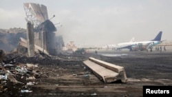 Planes are seen near a section of a damaged building (L) at Jinnah International Airport, after Sunday's attack by Taliban militants in Karachi, June 10, 2014. 