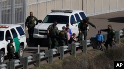 FILE - A woman and children are ushered into cars by U.S. Border Patrol agents after crossing illegally over the border wall into San Diego, Calif., as seen from Tijuana, Mexico, Dec. 9, 2018.