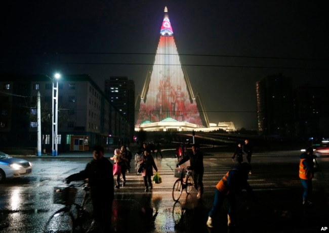 People cross a street as pyramid-shaped Ryugyong Hotel is seen in the background in Pyongyang, North Korea, Dec. 18, 2018.