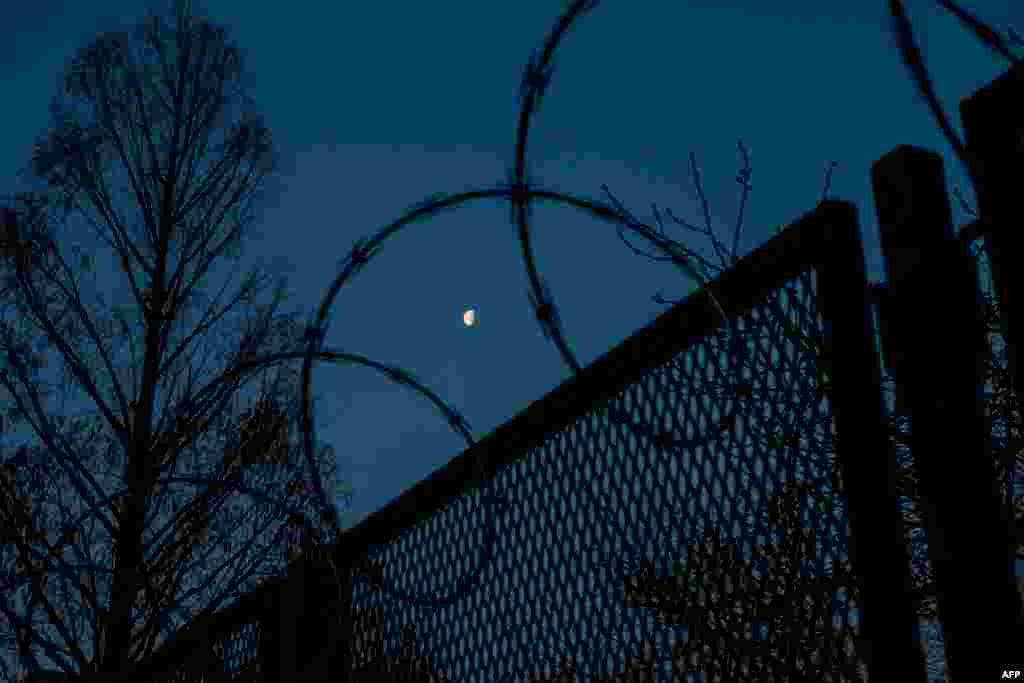 La luna se ve entre la cerca de alambre de p&#250;as que rodea el Capitolio de Estados Unidos antes del amanecer el 4 de marzo de 2021 en Washington, DC.