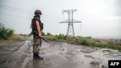 FILE - A Ukrainian serviceman stands near an electricity transmission tower outside the town of Zolote, some 60 km west of Luhansk city, Luhansk region, eastern Ukraine, Aug. 16, 2015. Ukraine's government announced Monday it will cut off power to rebel-held parts of Luhansk region because of millions in unpaid bills.