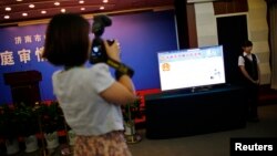A journalist takes pictures near a television screen displaying the Weibo page of Jinan Intermediate People's Court, at the court's media center during the trial of Bo Xilai in Jinan, Shandong province, Aug. 22, 2013.