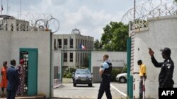 Des drapeaux français flottent en berne derrière un policier faisant un geste au départ du Premier ministre ivoirien après avoir signé un livre de condoléances à l'ambassade de France à Abidjan, le 15 juillet 2016.