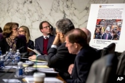 Democratic Sen. Dianne Feinstein, left, and several Senate colleagues look at a poster depicting an example of a misleading internet ad as representatives of Facebook, Twitter and Google testify during hearing on Capitol Hill in Washington, Oct. 31, 2017.