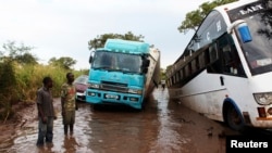 Des passagers se tiennent sur le bord de la route inondées sur la portion de la frontière entre le Soudan du sud et l'Ouganda, le 27 août 2013.