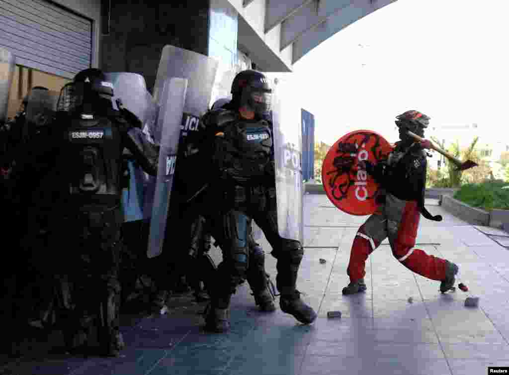 A demonstrator raises an axe towards riot police during anti-government protests, as Colombia marks Independence Day in Bogota, July 20, 2021.
