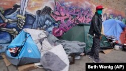 Sotero Cirilo stands near the tent, left, where he sleeps next to other homeless people in the Queens borough of New York, Wednesday, April 14, 2021.