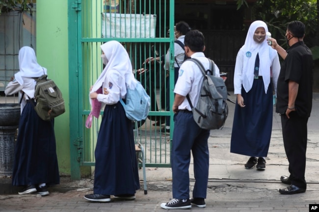 Seorang penjaga keamanan memeriksa suhu tubuh seorang siswa sebelum memasuki sekolahnya pada 13 Juli 2020. (Foto: AP/ACHMAD Ibrahim)