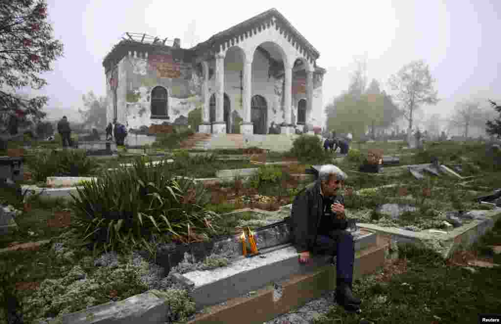 A Kosovo Serb man sits next to a vandalized grave in the ethnically divided Kosovo town of Mitrovica. Serbs from the north of Mitrovica crossed the river into the mainly Albanian south to pay respects to lost loved ones on the winter "Zadusnice" -- the Serbian Orthodox equivalent of All Souls' Day -- at the Orthodox cemetery.