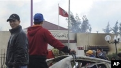 People stand outside an official building with a charred car in M'nihla, outside Tunis, Jan.13, 2011. Sporadic sounds of clashes and rounds of gunfire echoed in the suburbs of Tunisia's capital early Thursday as youths defied a government curfew order ai