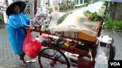 Seorang ibu tengah mendorong gerobak jualannya di sebuah area perumahan di Jakarta (VOA/Iris Gera). Pemerintah menjamin cukup tersedianya bahan kebutuhan pangan bagi seluruh wilayah tanah air di musim penghujan seperti sekarang ini.