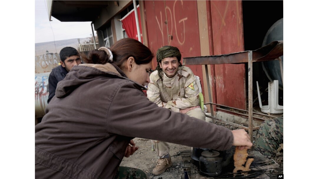 FILE - A female fighter from the Turkey-based Kurdish Workers' Party sits with fighters from the Syria-based People's Protection Units (YPG) on the outskirts of the town of Sinjar, northern Iraq, on Jan. 29, 2015.