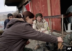 FILE - A fighter from the Syria-based People's Protection Units (YPG) smiles at a female fighter from the Turkey-based Kurdish Workers' Party at their base while they sit around a fire on the outskirts of the town of Sinjar, northern Iraq, on Jan. 29, 2015.