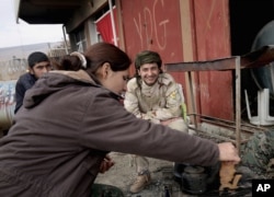 FILE - A female fighter from the Turkey-based Kurdish Workers' Party sits with fighters from the Syria-based People's Protection Units (YPG) on the outskirts of the town of Sinjar, northern Iraq, on Jan. 29, 2015.