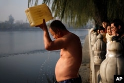 FILE - People in winter clothes watch a Chinese man pouring icy water on himself as he prepares to swim in the half-iced water at Shichahai Lake in Beijing on Nov. 29, 2015.