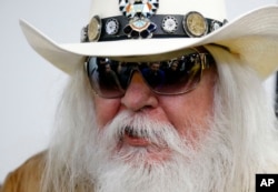 FILE - Reporters are reflected in the sunglasses of Leon Russell as he answers a question at a news conference in Tulsa, Oklahoma, Jan. 29, 2013.